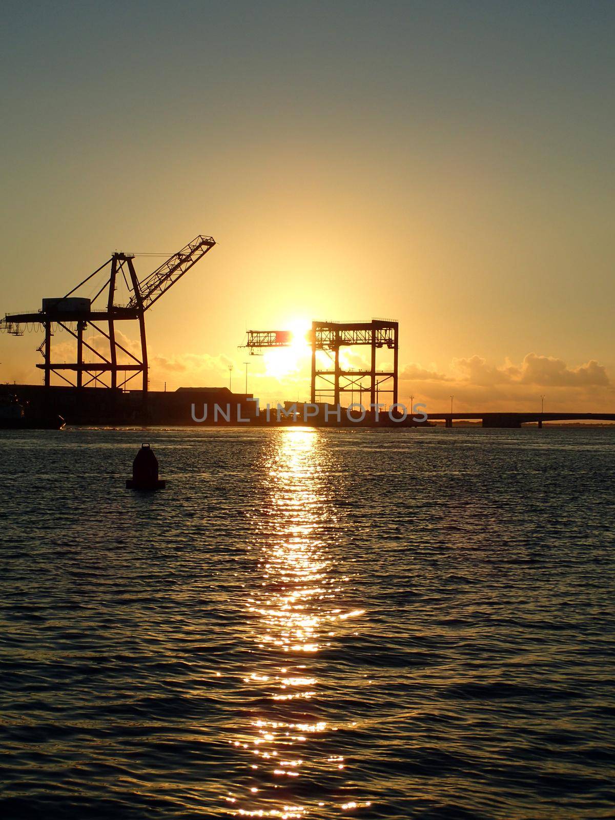 Sunset through Hoisting cranes at container cargo terminals with Bridge on Sand Island on Oahu, Hawaii.