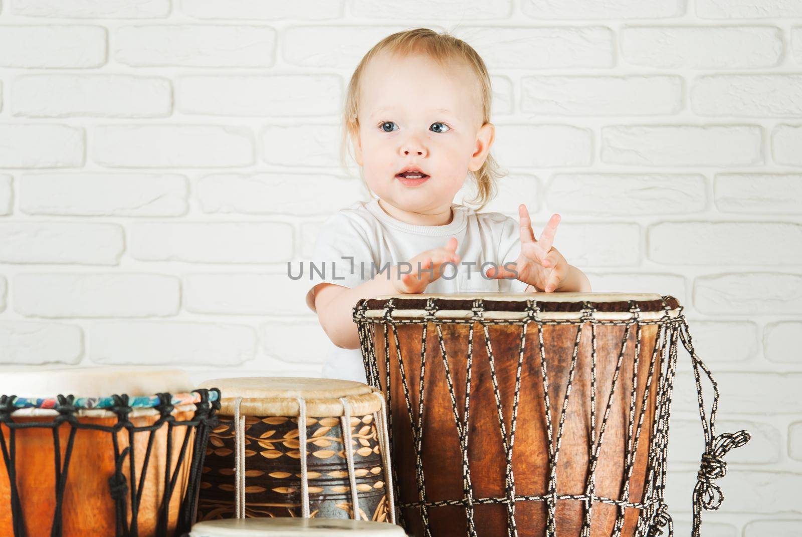 Cute toddler baby playing ethnic drums next to bricks wall