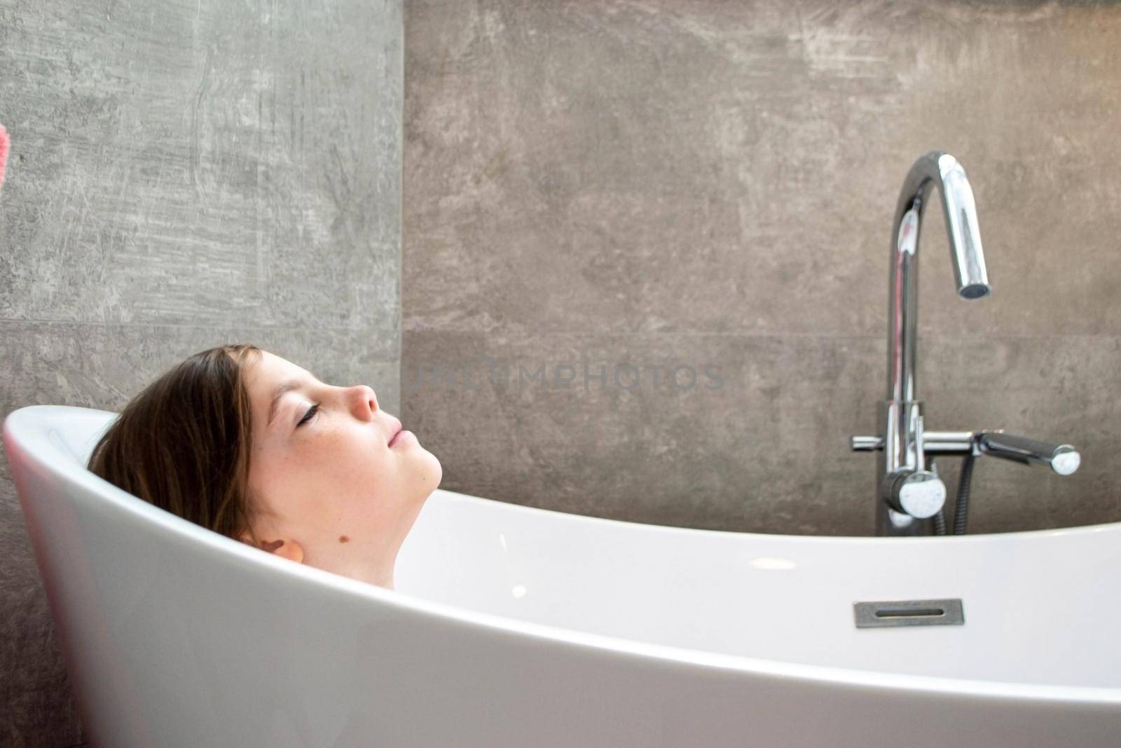 Relaxed young girl model wears towel wrapped on head, feels refreshed after taking shower, has healthy clean soft skin, poses in cozy bathroom. Girl, beauty and hygiene concept. High quality photo