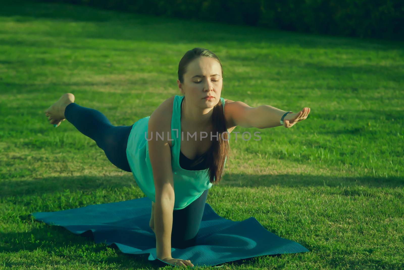 Young woman doing yoga at green grass in the park in the morning