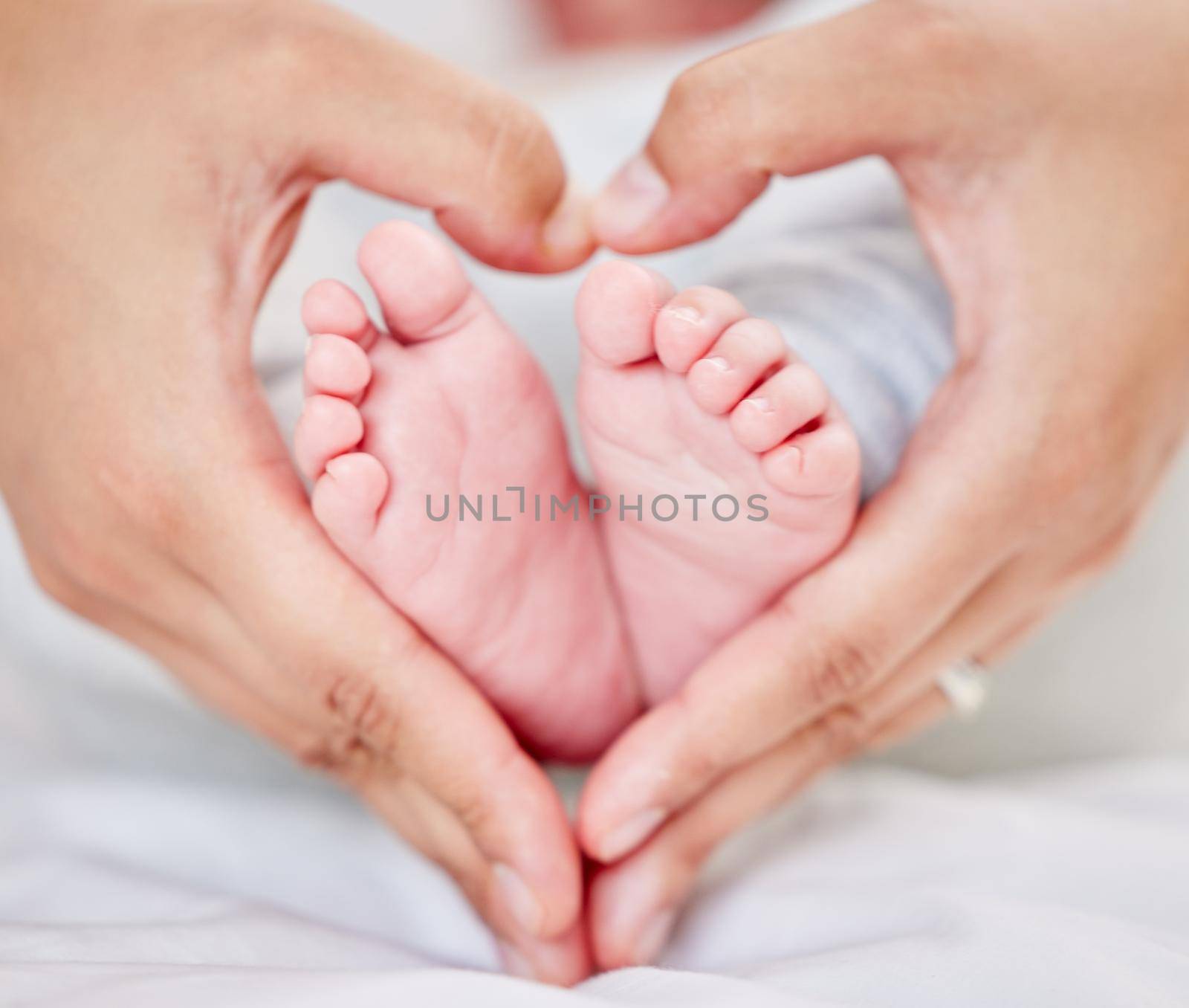 Closeup of hands of a parent forming a heart shape around tiny newborn baby feet. Mother loving her little baby. Small baby resting in its nursery while parent holds its feet