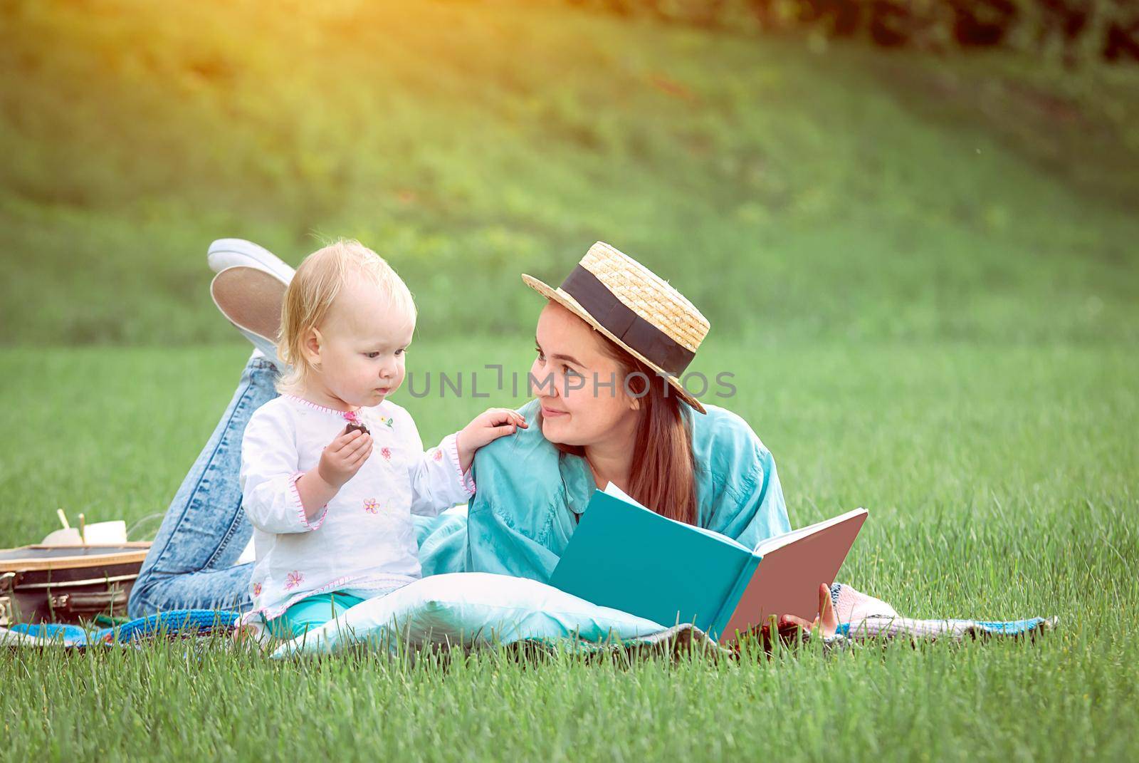 Mother is reading book for baby girl lying on the grass in the park. High quality photo