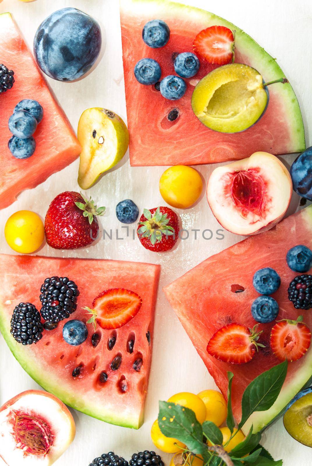 variation of summer berries and fruits cutted in pieces on white wooden background