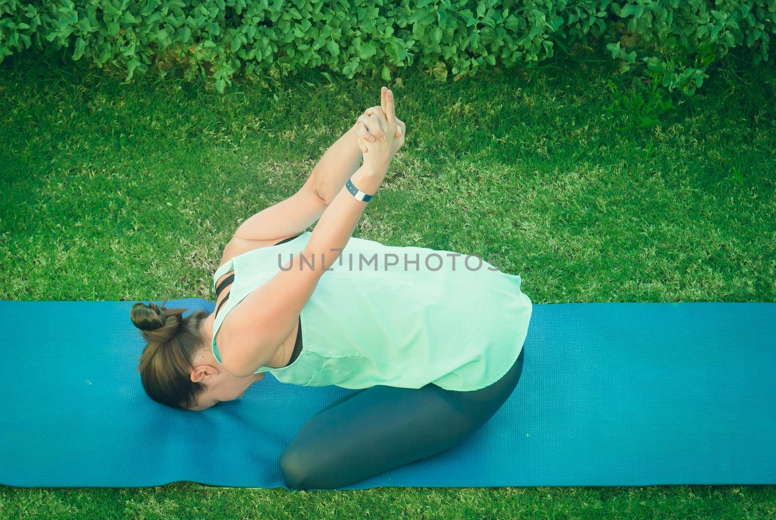 Young woman doing yoga at green grass in the park in the morning