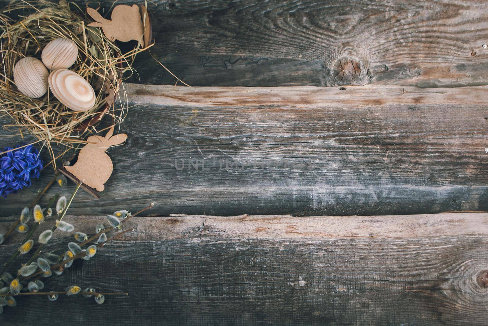 Easter decoration with wooden eggs in bascket and straw on wooden background