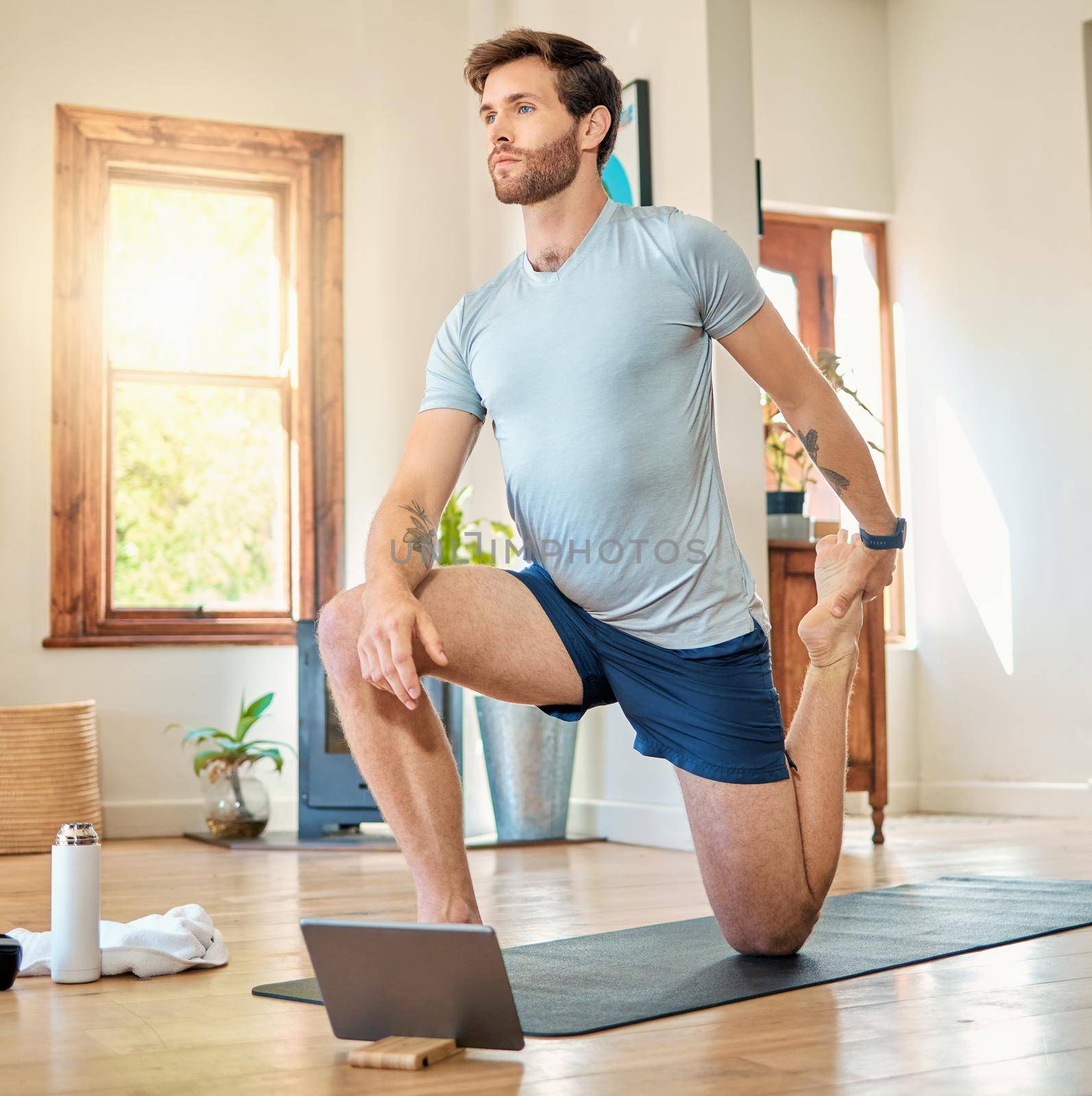 One fit young caucasian man stretching legs with lunge bodyweight exercise and holding foot while training with online tutorial on digital tablet at home. Guy gaining muscle, endurance, balance and core strength during yoga workout.