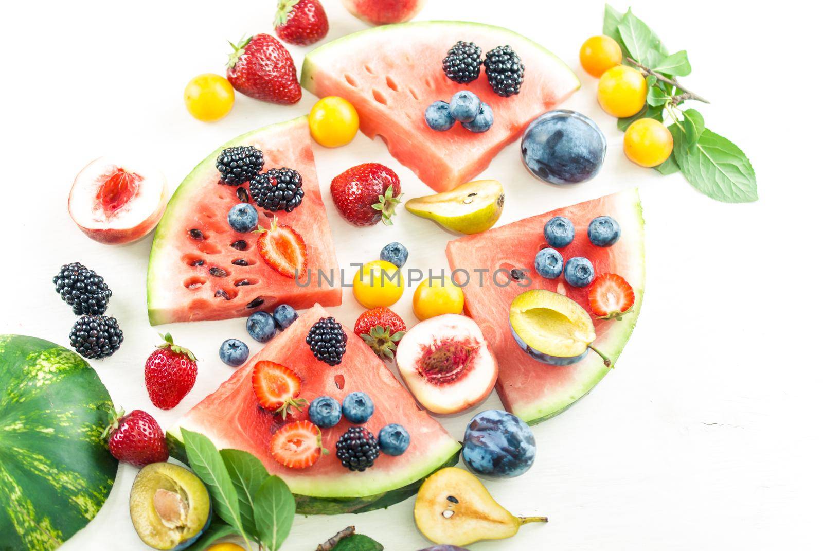 variation of summer berries and fruits cutted in pieces on white wooden background