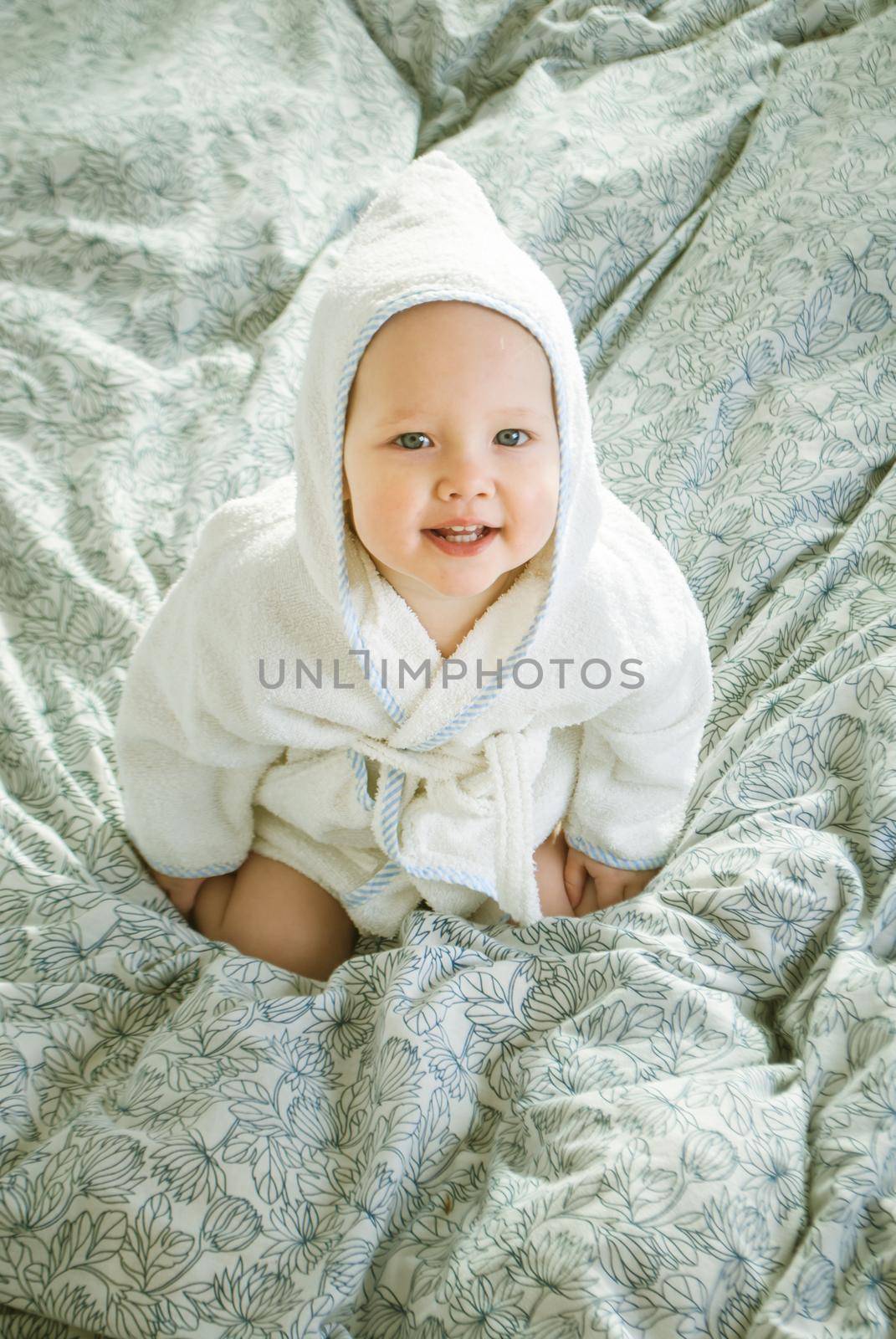 cute babygirl in parents bed in bathrobe and hood on head