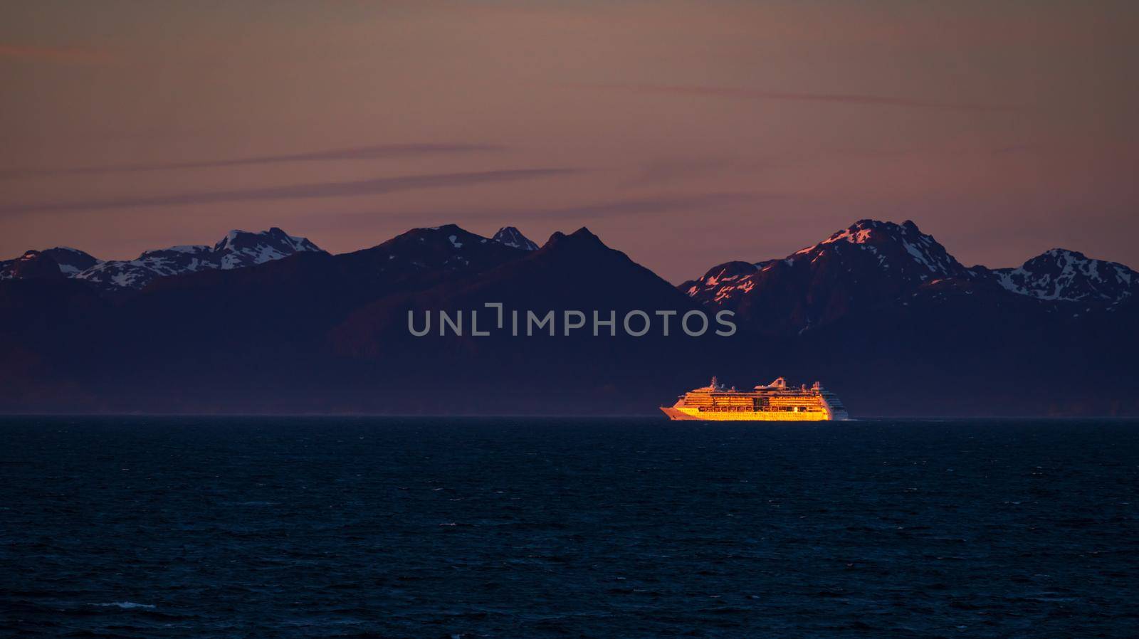 Late evening sunset illuminates a very distant cruise ship against the snowy Alaska coastline