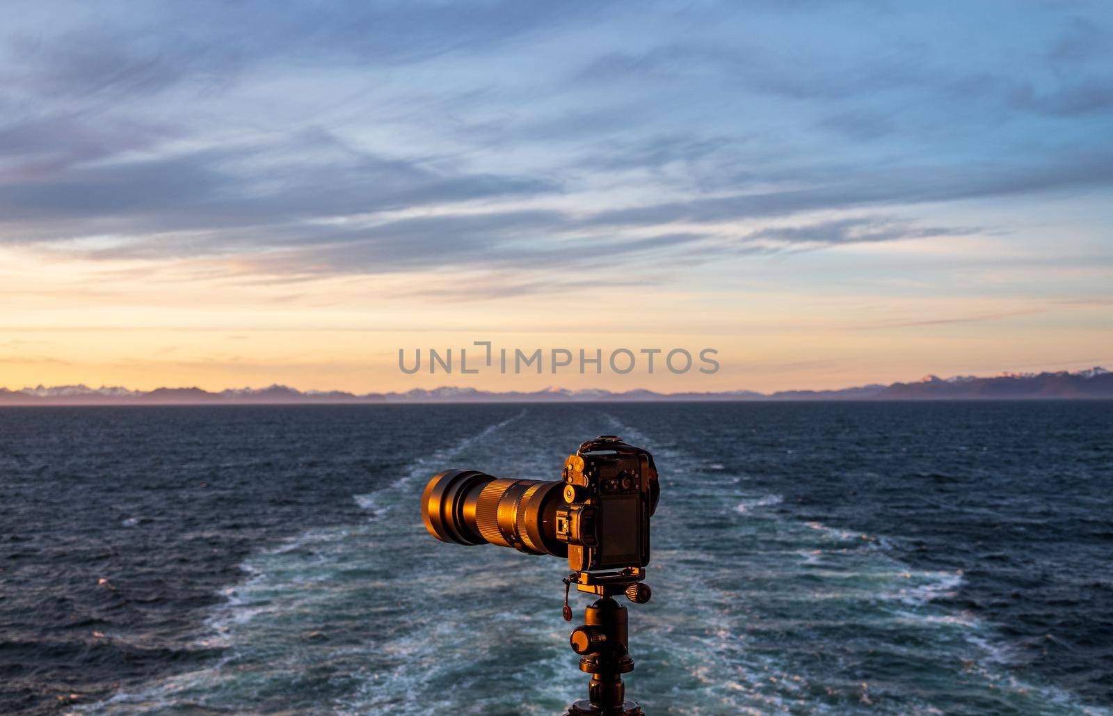 Professional dslr on tripod on back of cruise ship sailing away from Alaska coast leaving wake