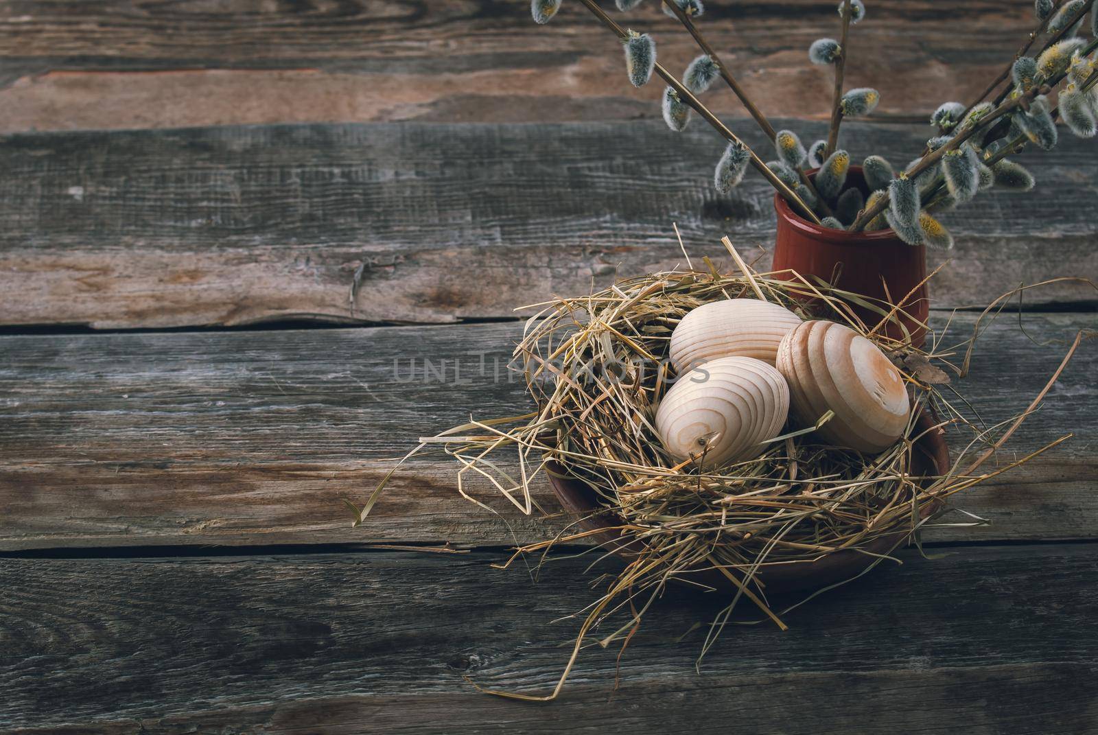 Easter decoration with wooden eggs in bascket and straw on wooden background