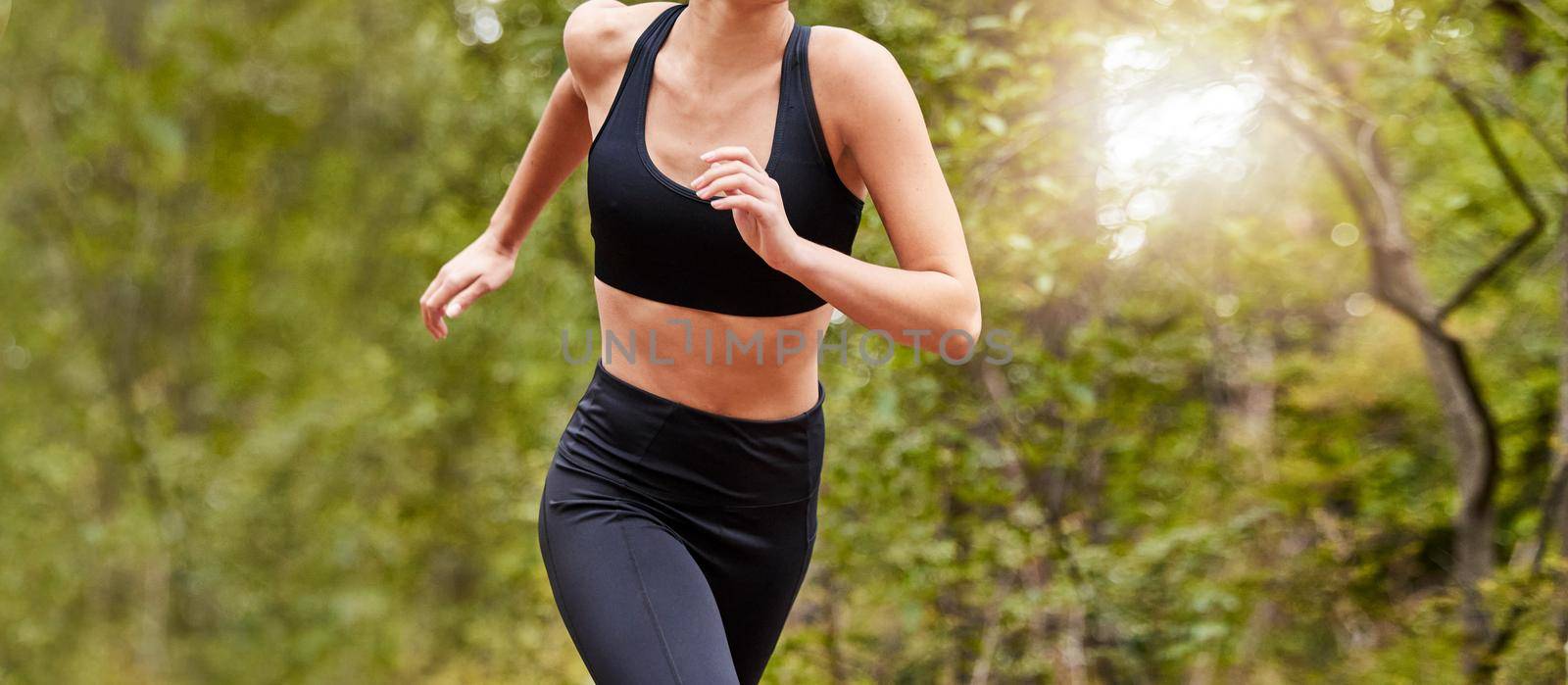 Close up of a womans fit body wearing workout clothes while out for a run at a park or in nature on a sunny day. Woman exercising and living a healthy lifestyle by YuriArcurs