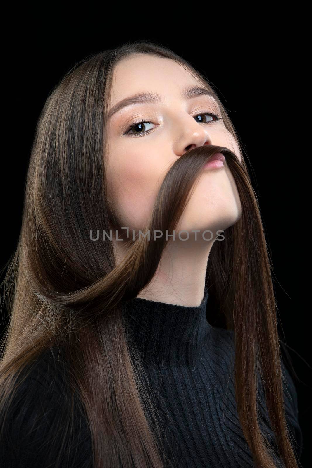 A beautiful girl with long hair fooling around in front of the camera. Makes a mustache out of hair.