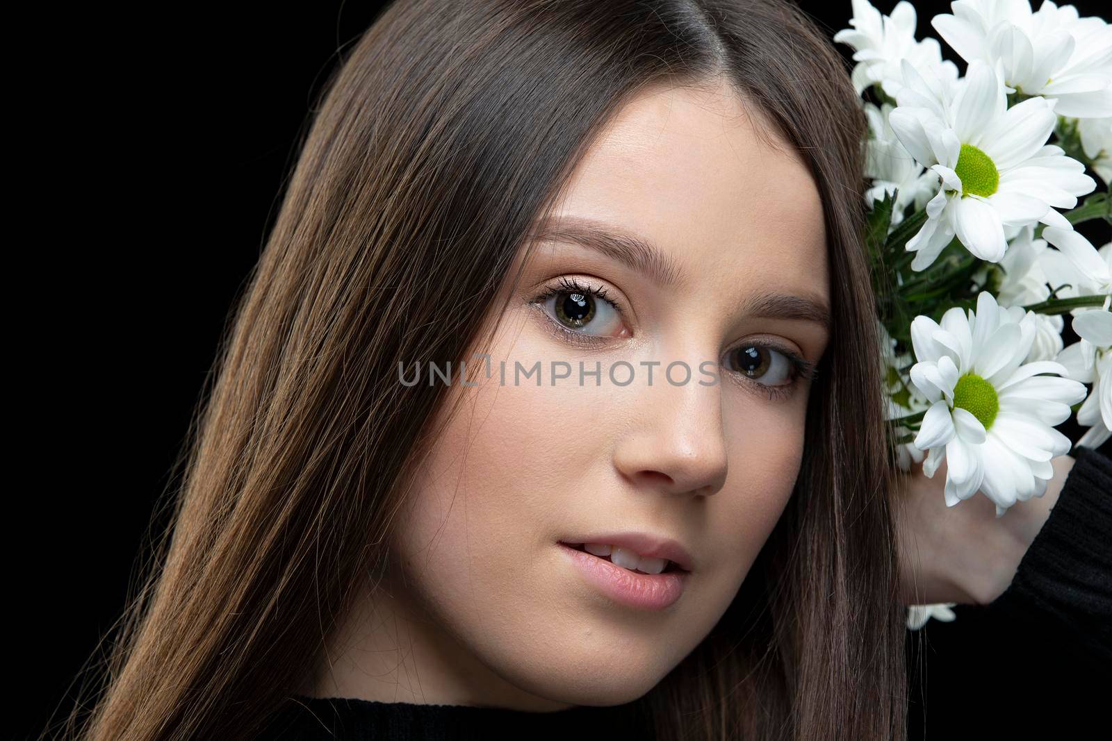 A beautiful young girl with natural beauty with long smooth hair holds a bouquet of white chrysanthemums.