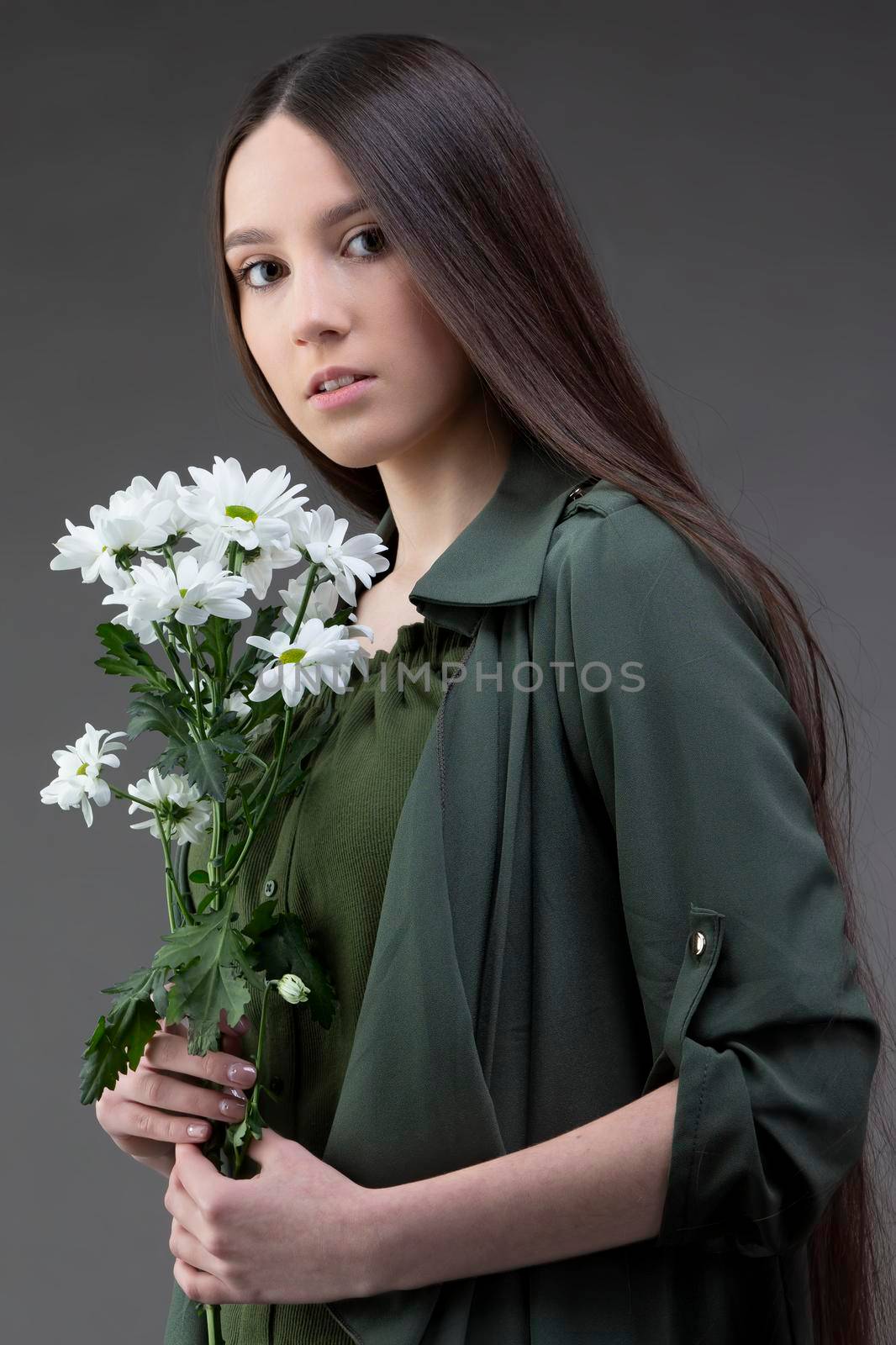 A beautiful young girl with natural beauty with long smooth hair holds a bouquet of white chrysanthemums.