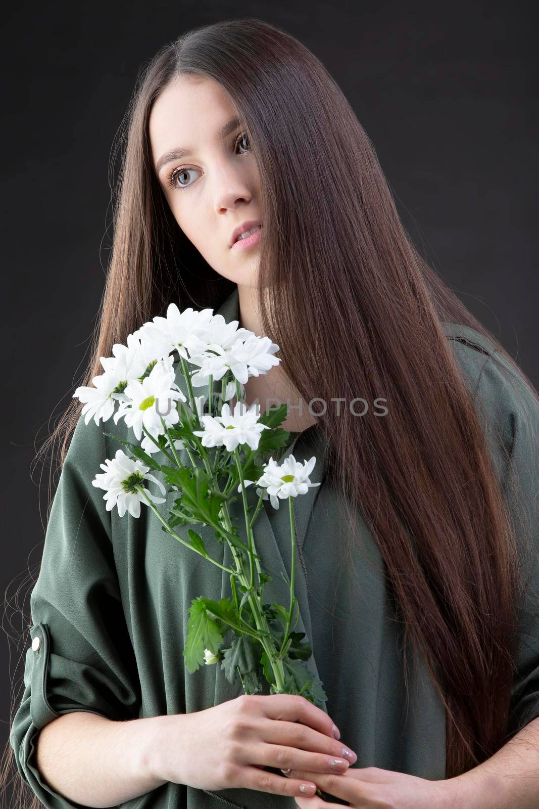 A beautiful young girl with natural beauty with long smooth hair holds a bouquet of white chrysanthemums.