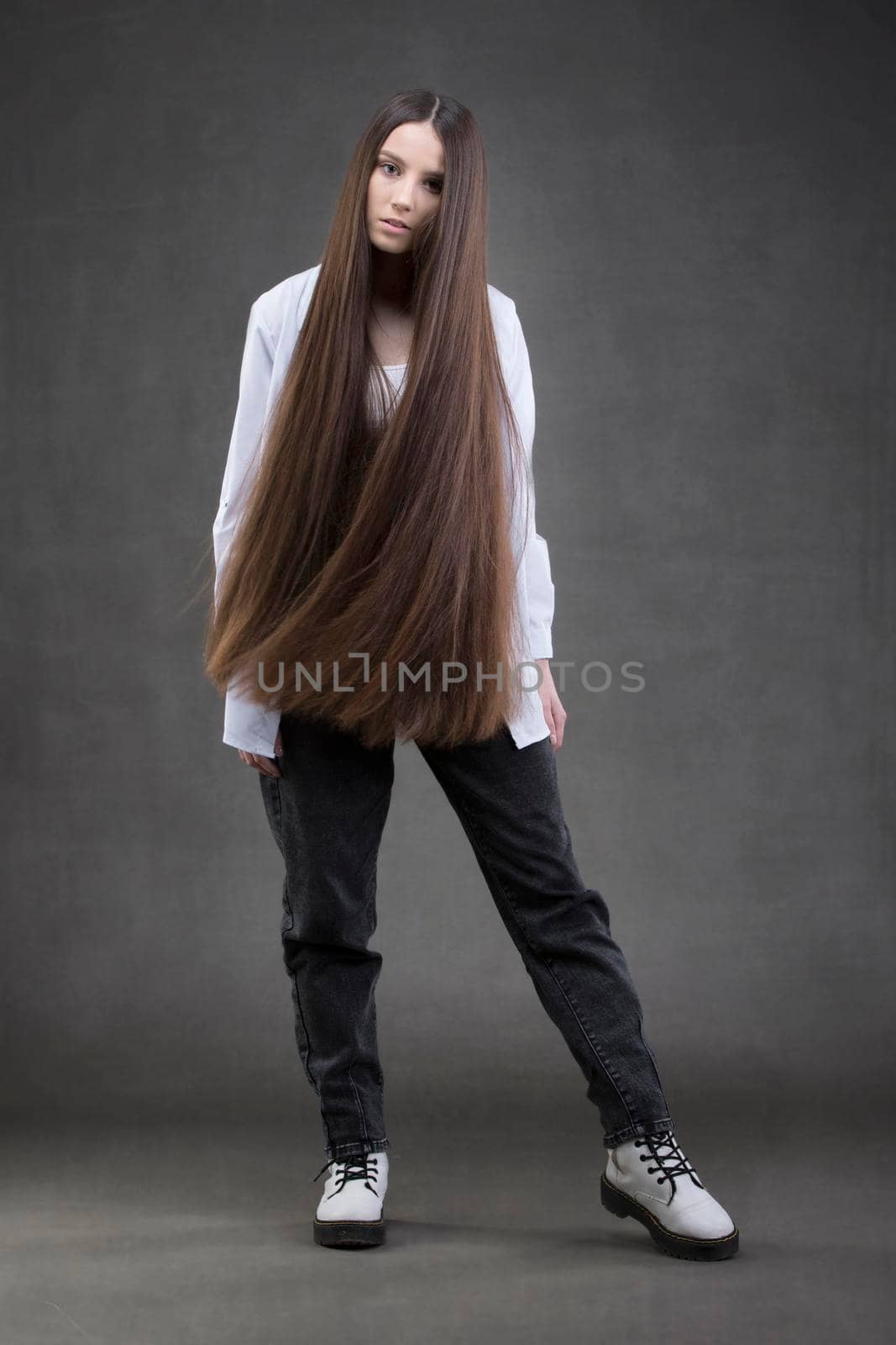 A beautiful girl with very long hair in full growth on a gray background.