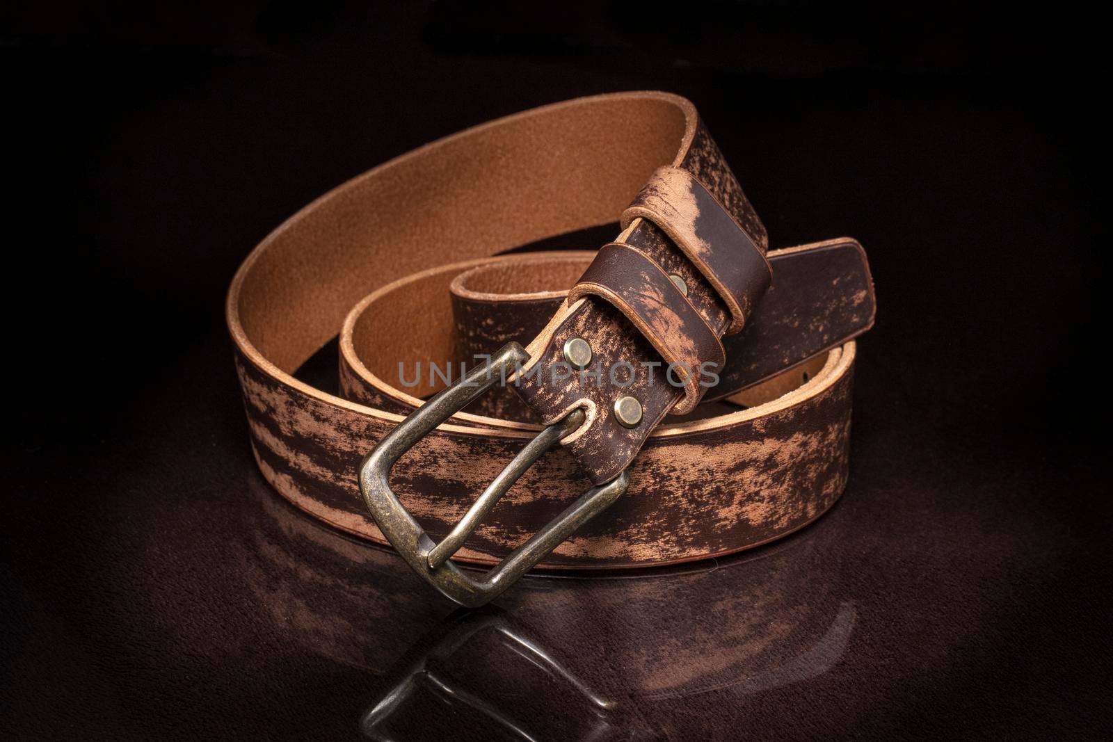 Brown leather belt with scuffs and a metal buckle on a dark background.
