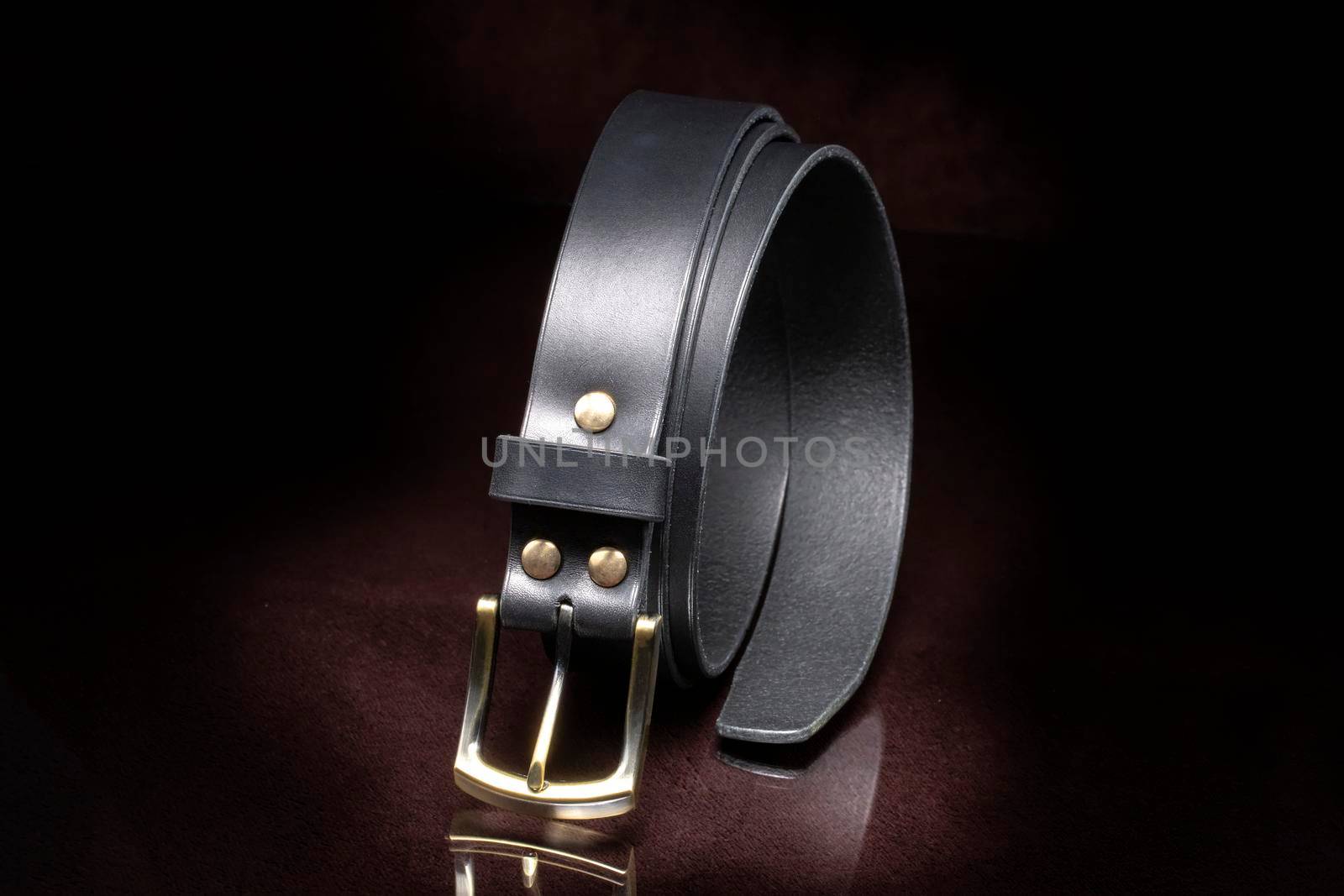 Leather belt with a metal buckle close-up on a dark background.