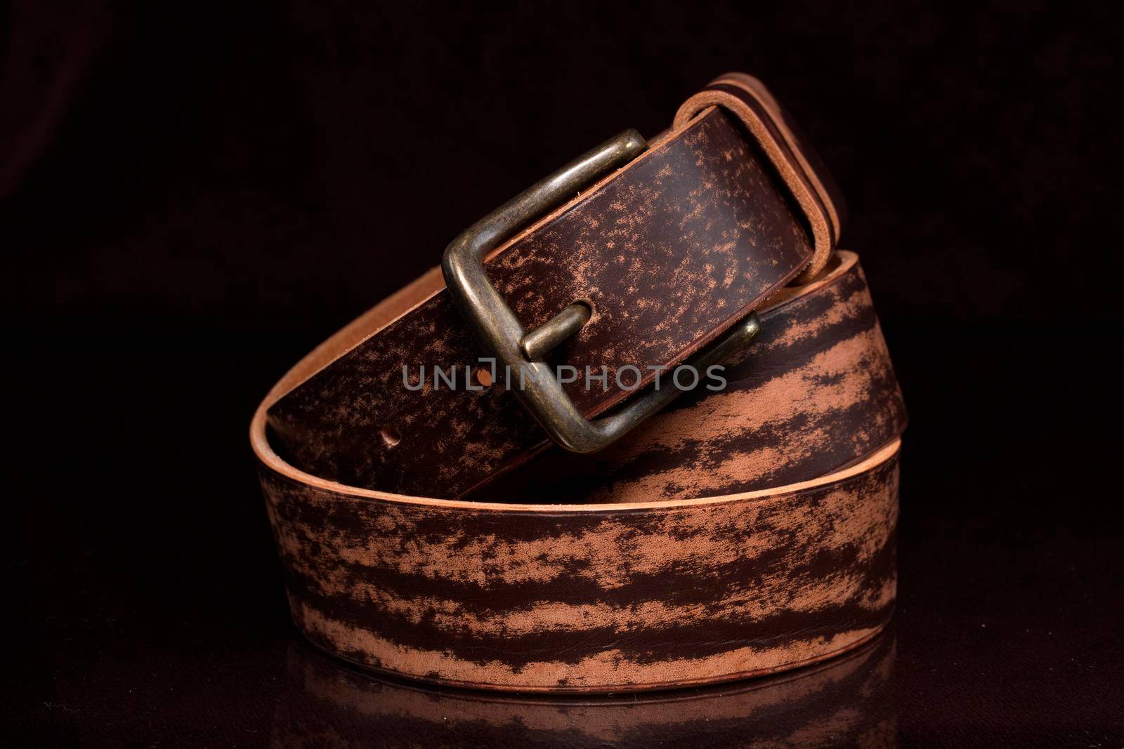 Brown leather belt with scuffs and a metal buckle on a dark background.