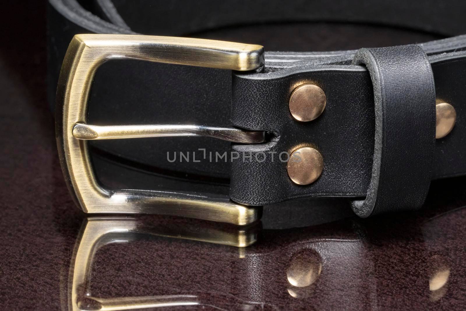 Leather belt with a golden buckle on a dark background close-up.