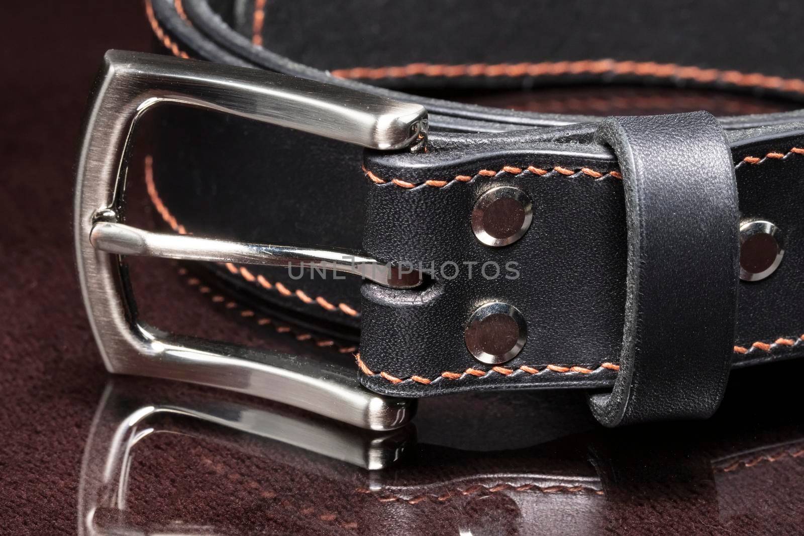 Black leather belt with a metal buckle on a dark background close-up.