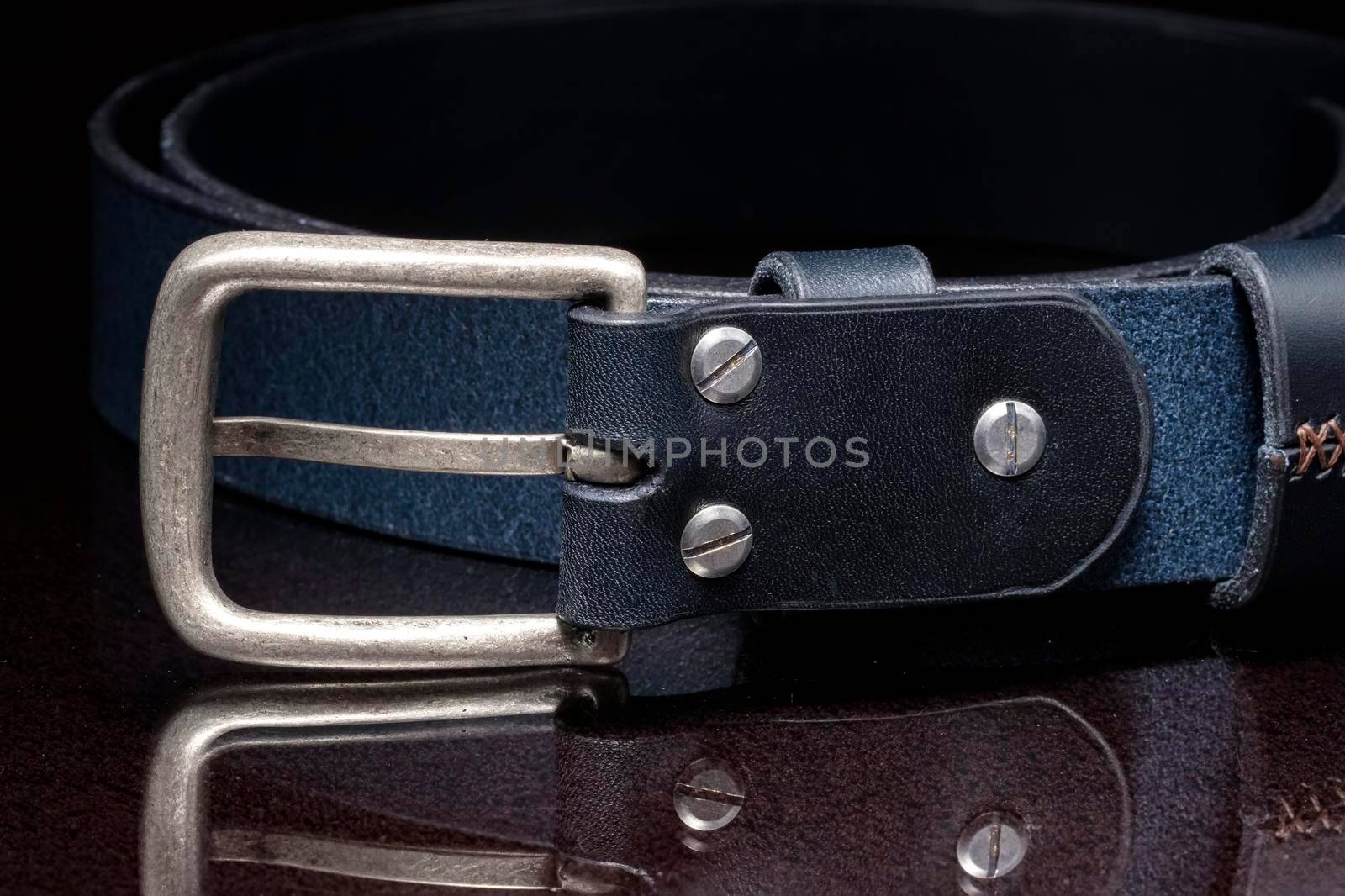 Leather belt with a metal buckle close-up on a dark background.