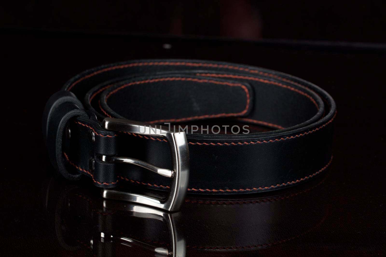 Black leather belt with a metal buckle on a dark background close-up.