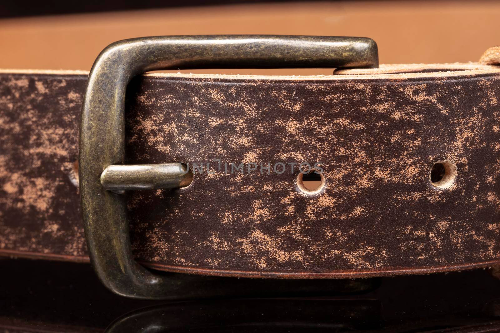 Brown leather belt with scuffs and a metal buckle on a dark background.