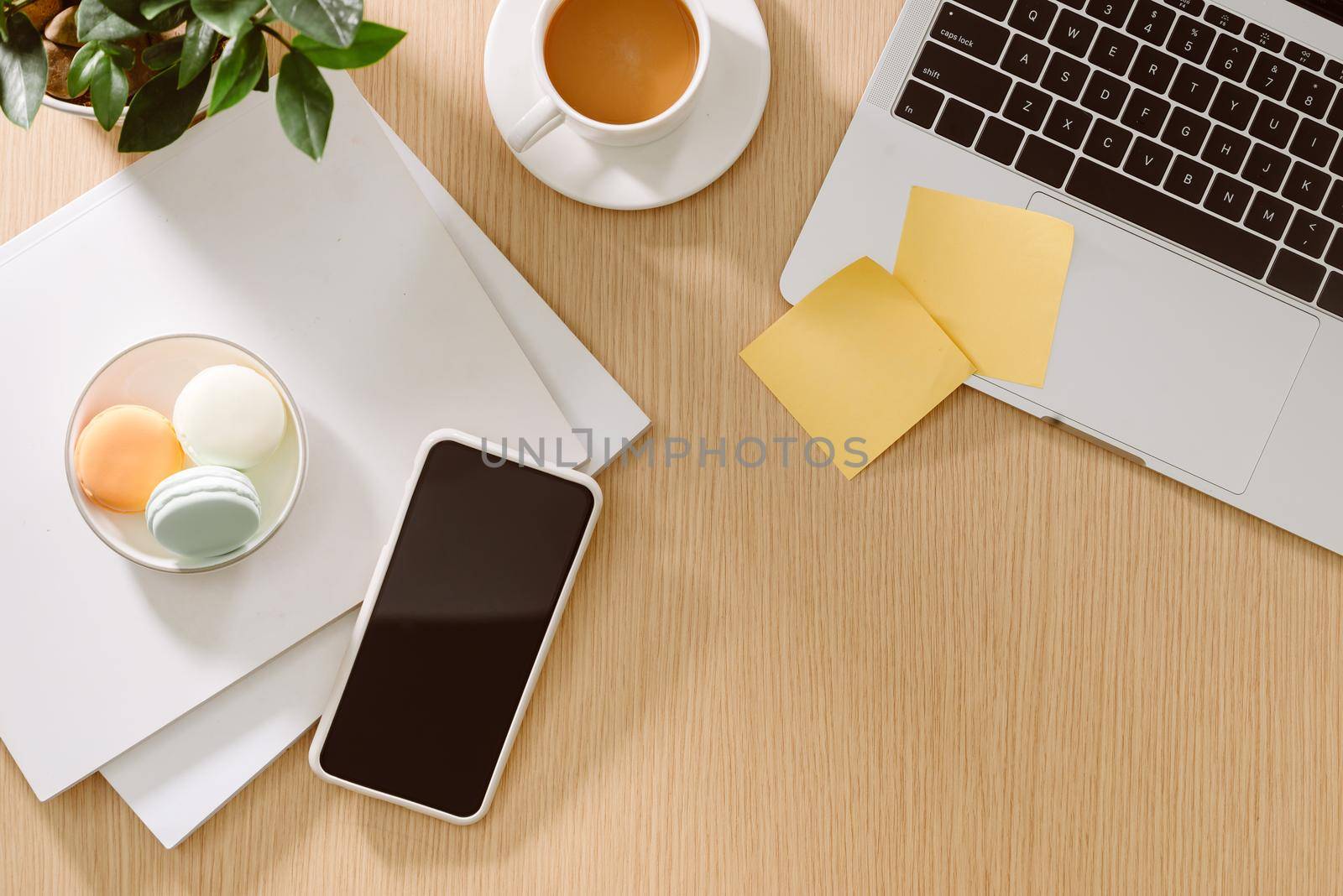 Trendy feminine home office workspace. White office desk. Laptop, coffee cup and macaroons, phone, notebook, pencil. Flat lay, top view, copy space