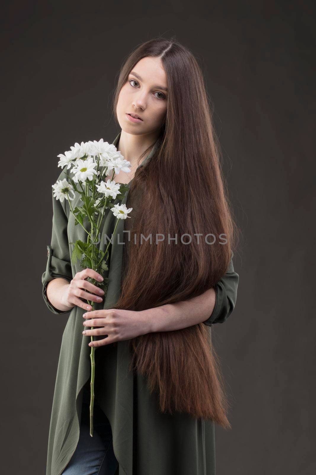 A beautiful young girl with natural beauty with long smooth hair holds a bouquet of white chrysanthemums.