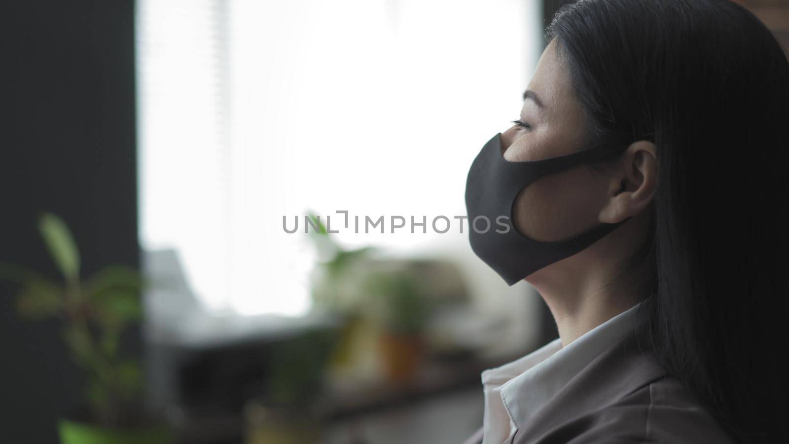 Profile View Of Young Asian Business Woman In Black Protective Mask, Brunette Woman Looks At Window Standing In Office Raised Her Head High, Copy Space At Left Side, Virus Outbreak Concept