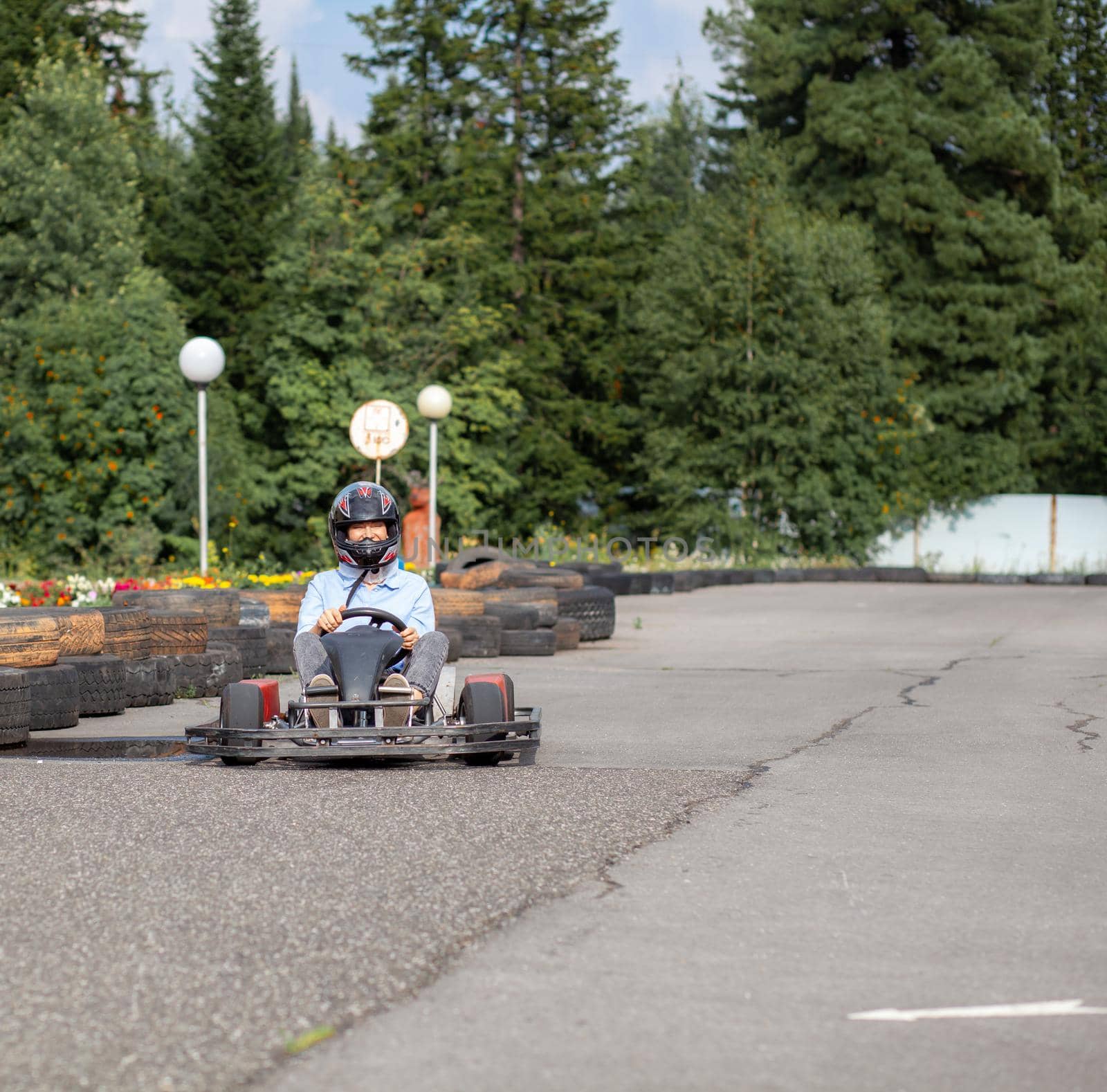 A girl or a woman in a hard hat rides a go-kart on a special track fenced with rubber wheels. Active recreation and sports on transport. Preparation and training for competitions. 