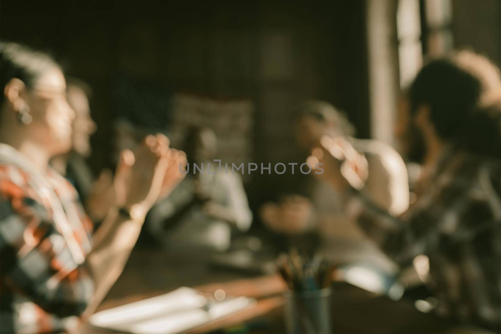 Multi-Ethnic Business Team Of Freelancers In Casual Clothing Clapping Their Hands While Sitting At Table In Board Room, Abstract Defocused Image Of Unrecognizable Person Or Blurred Back