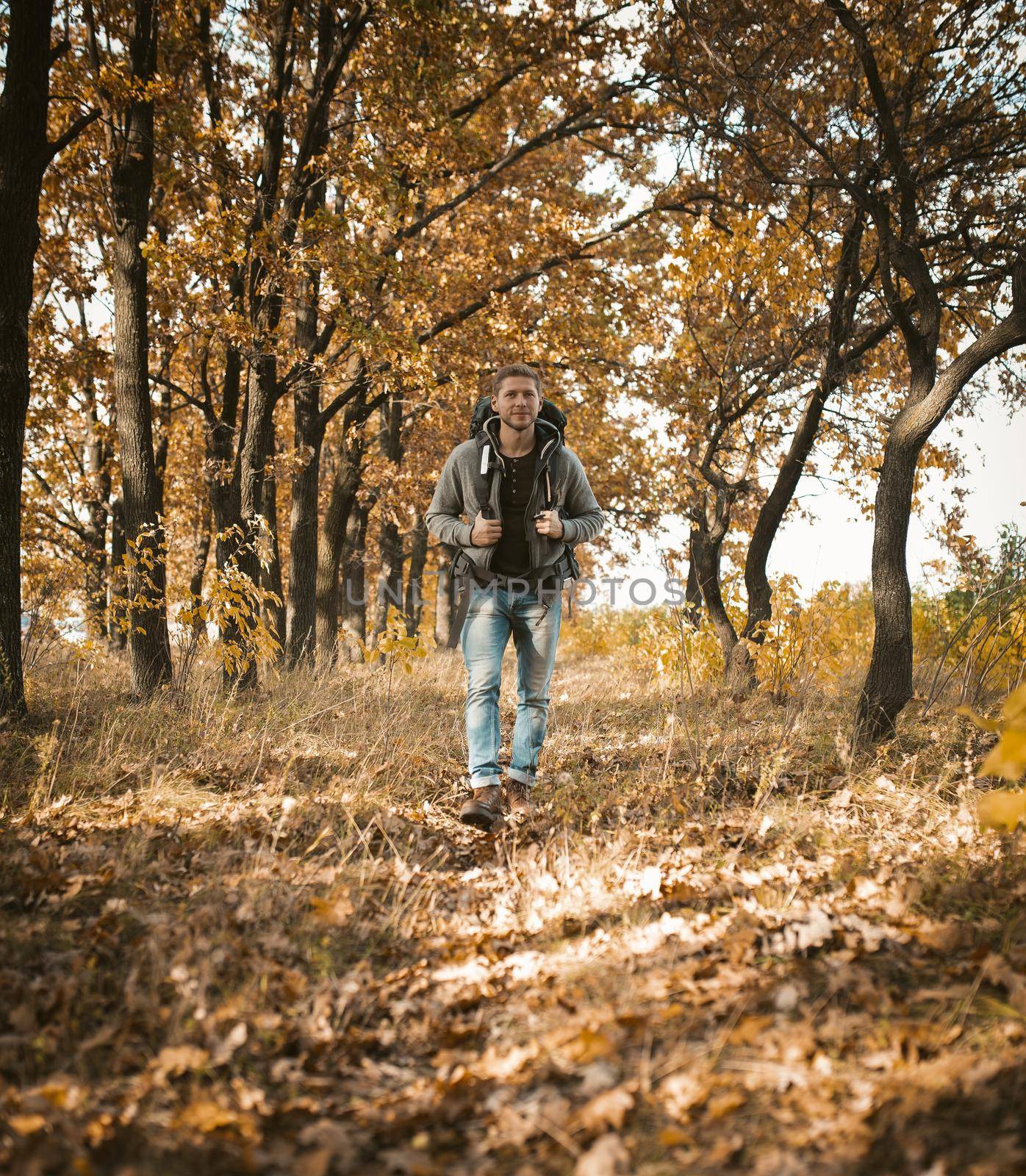 Young Traveler Walking Along In Autumn Forest, Happy Caucasian Man With Big Backpack Walks Along A Forest Path On Outskirts Of Field, He Admires The Beauty Of Nature Traveling Outdoors On Sunny Day