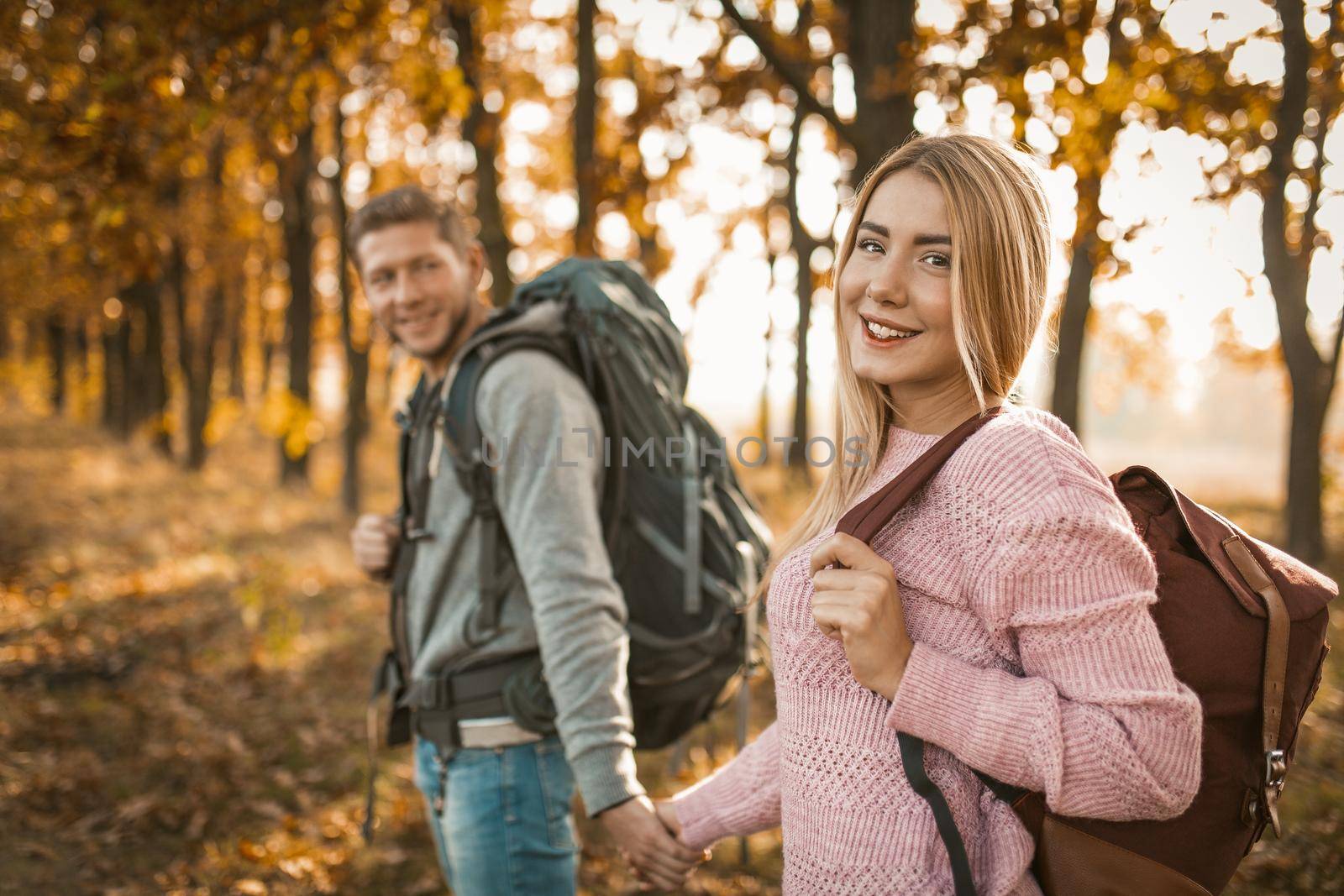 Beautiful Couple Walk Along A Forest Path, Focus On A Smiling Blonde Woman Looking At Camera, Young Man And Woman Traveling Outdoors In An Autumn Sunny Day
