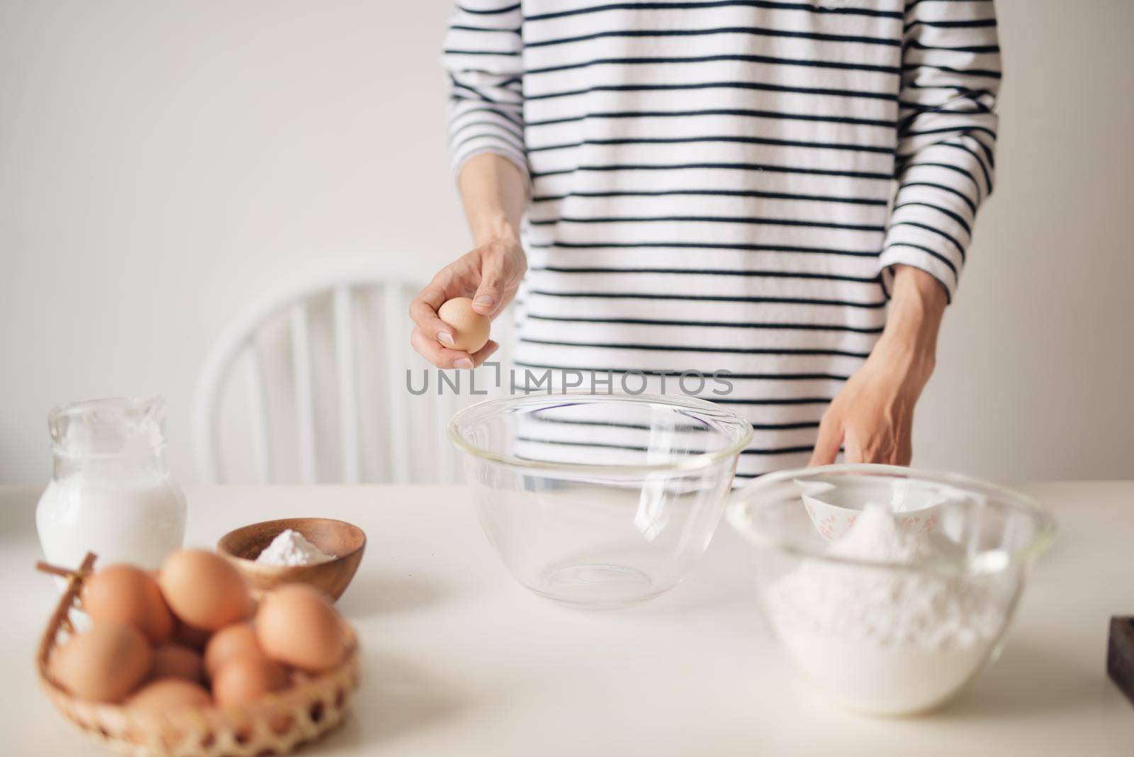 Horizontal shot of serious male wearing beige apron breaking egg into metal bowl by makidotvn
