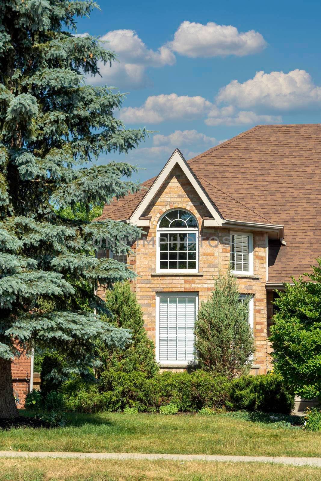 Fragment of a house with an attic and blue spruce under white clouds