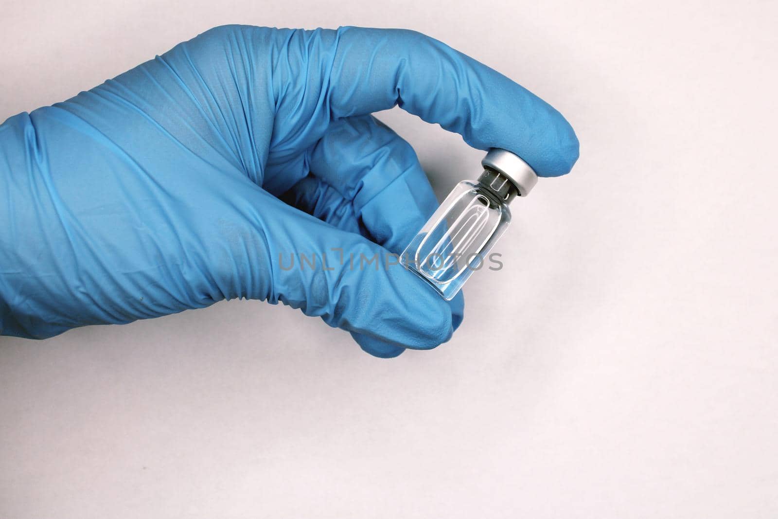 A hand in a blue medical glove close-up holding a vaccine against a light background. The concept of the fight against Covid19..