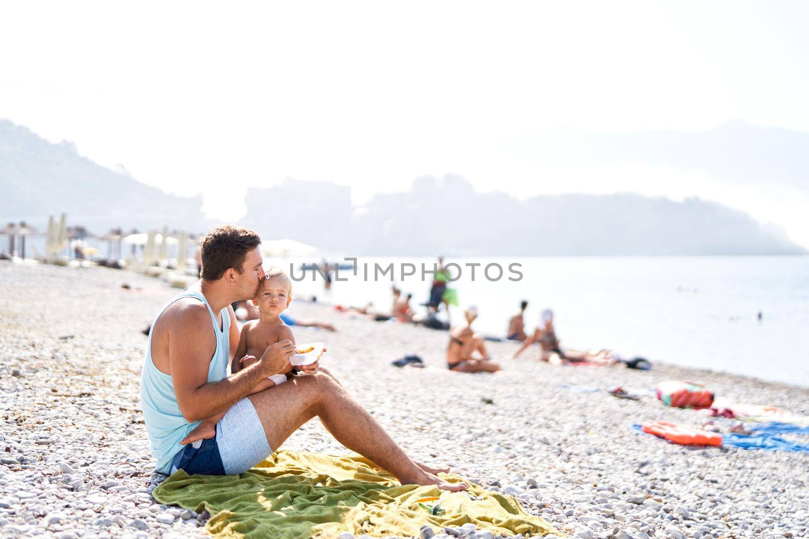 Dad kisses his little daughter while feeding on the beach. High quality photo