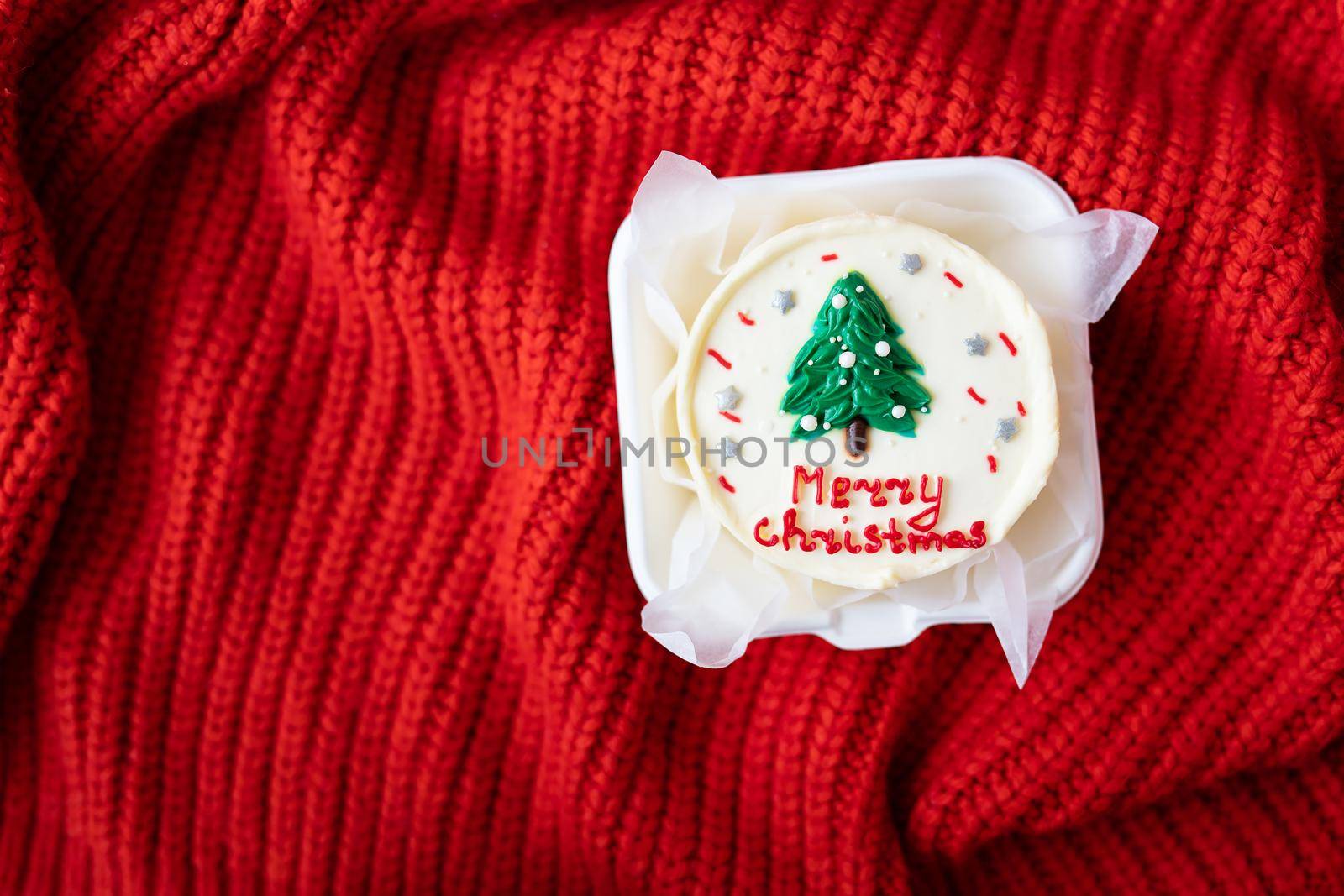 Christmas cake with the inscription merry christmas, decorated with icing, on a red background, top view