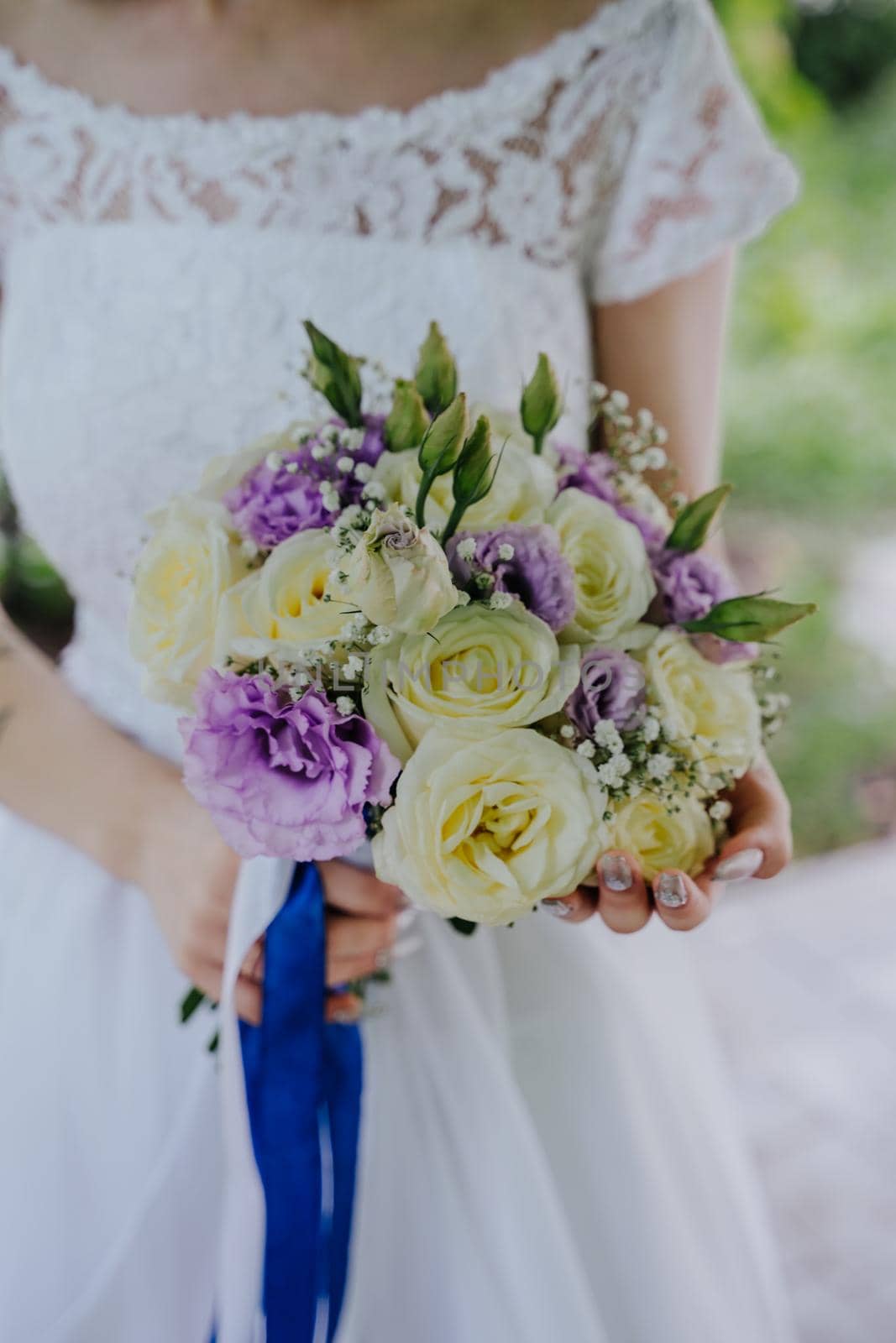 A beautiful and delicate bouquet in the hands of the bride. Bouquet with blue ribbons. Purple eustoma flowers, white roses and gypsophila twigs. Vertical photo.