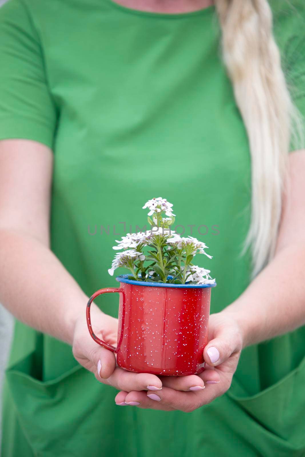 a blonde girl with long hair in a bright green dress holding a red mug with a bouquet of white flowers, portrait, High quality photo