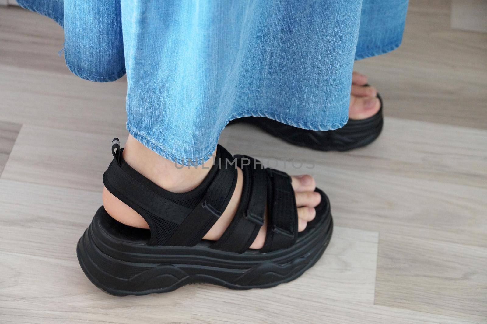 female legs in black bulky sandals close-up by Annado