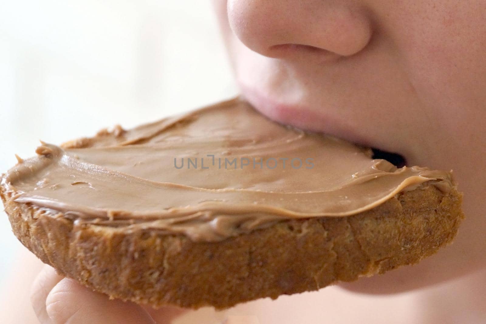 girl biting a sandwich with chocolate paste close up by Annado