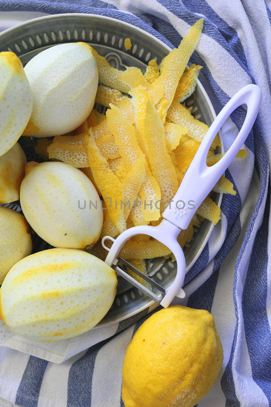 Lemon fruits and peeled strips for zest or making limoncello. Peeler, lemons and zest. Copy space, selected focus. Vertical image