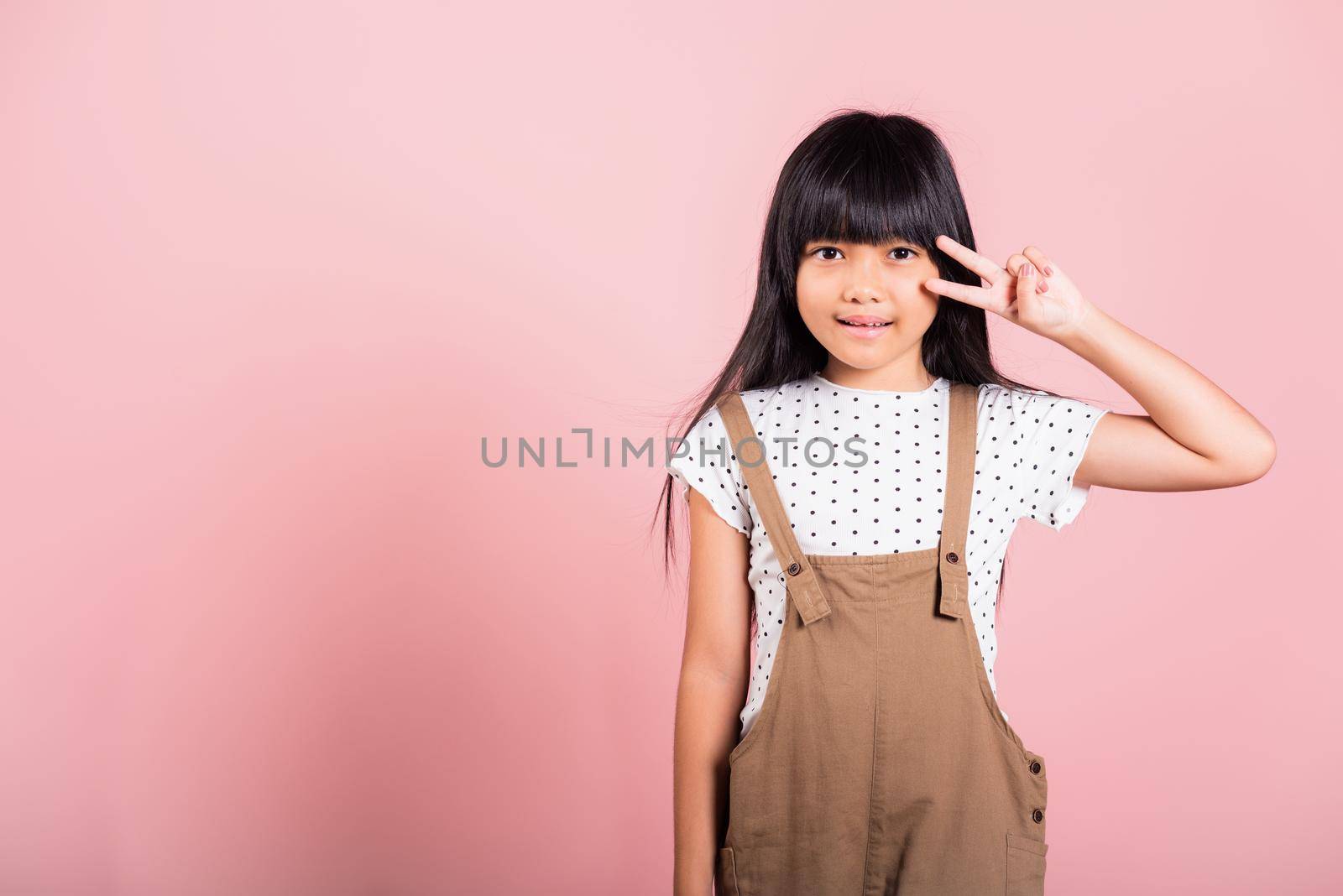 Asian little kid 10 years old show v-sign fingers gesture at studio shot isolated on pink background, Happy child girl lifestyle making victory symbol sign