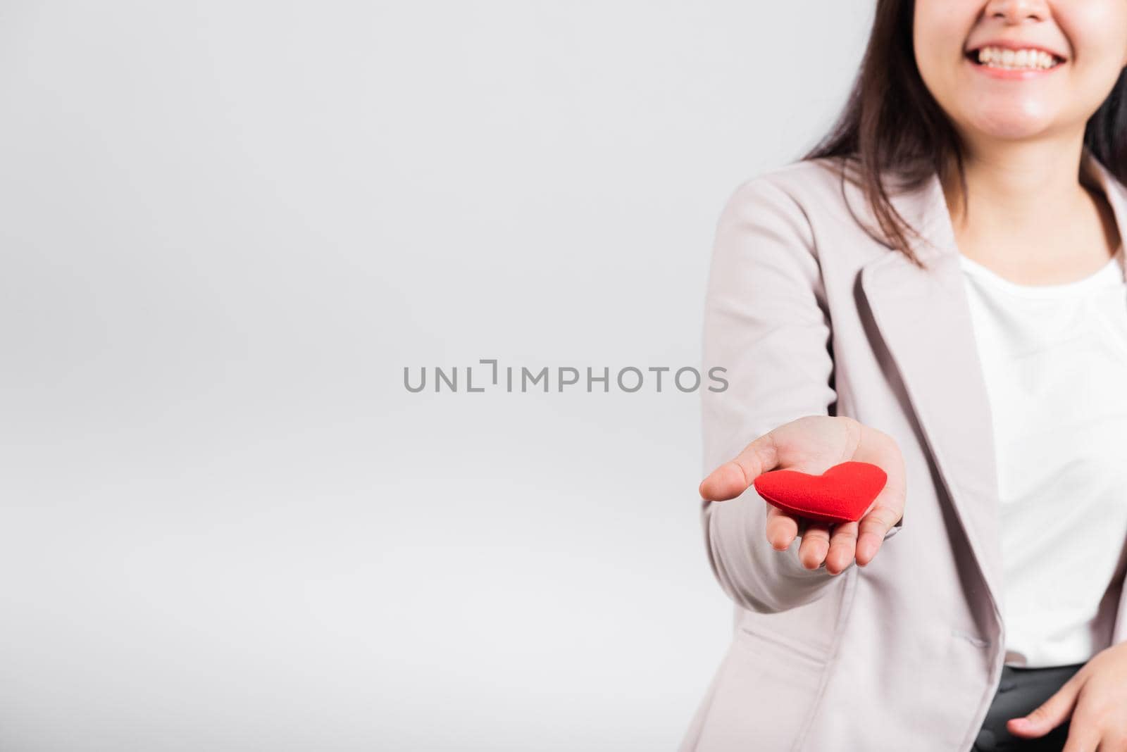 Smiling woman confidence showing holding red heart with her hand palm isolated white background, Asian happy portrait beautiful young female send love and happy valentine in studio shot, copy space