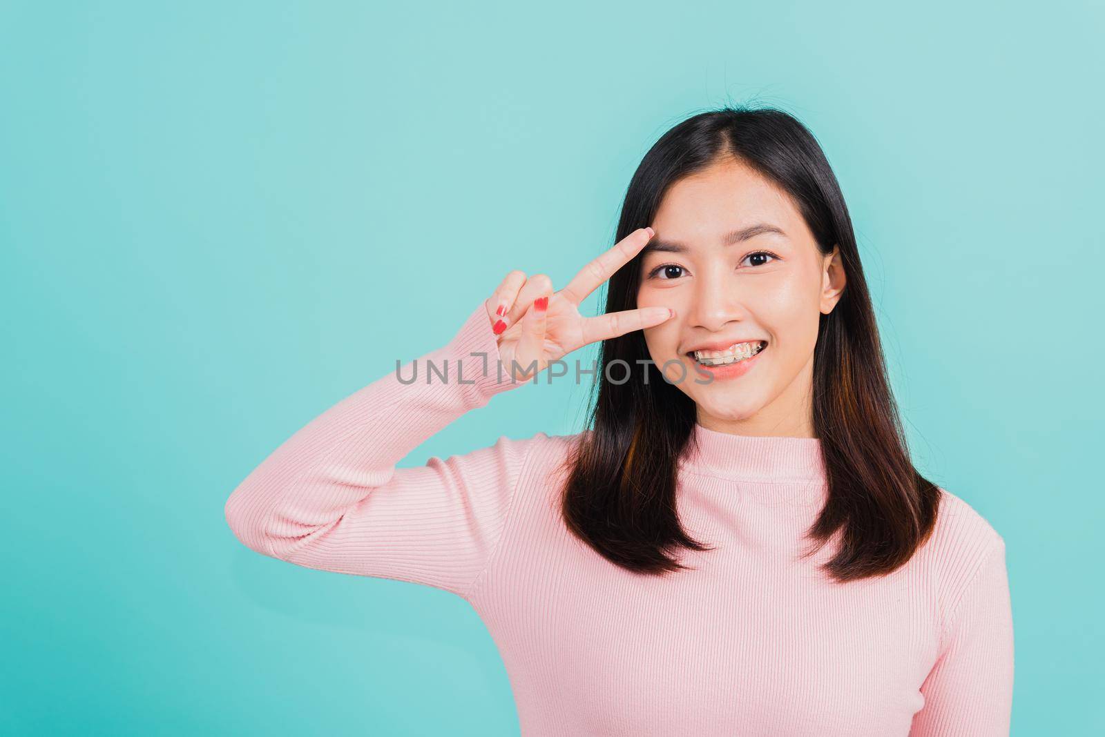 Asian beautiful woman smiling wear silicone orthodontic retainers on teeth showing v-sign victory finger near eye isolated on blue background, retaining after removable braces. Dental hygiene concept