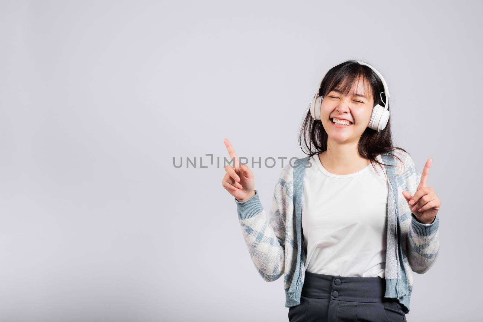 Woman excited smiling listening to music radio in bluetooth headphones and dancing with smartphone studio shot isolated white background, happy Asian young female Karaoke online app in mobile phone